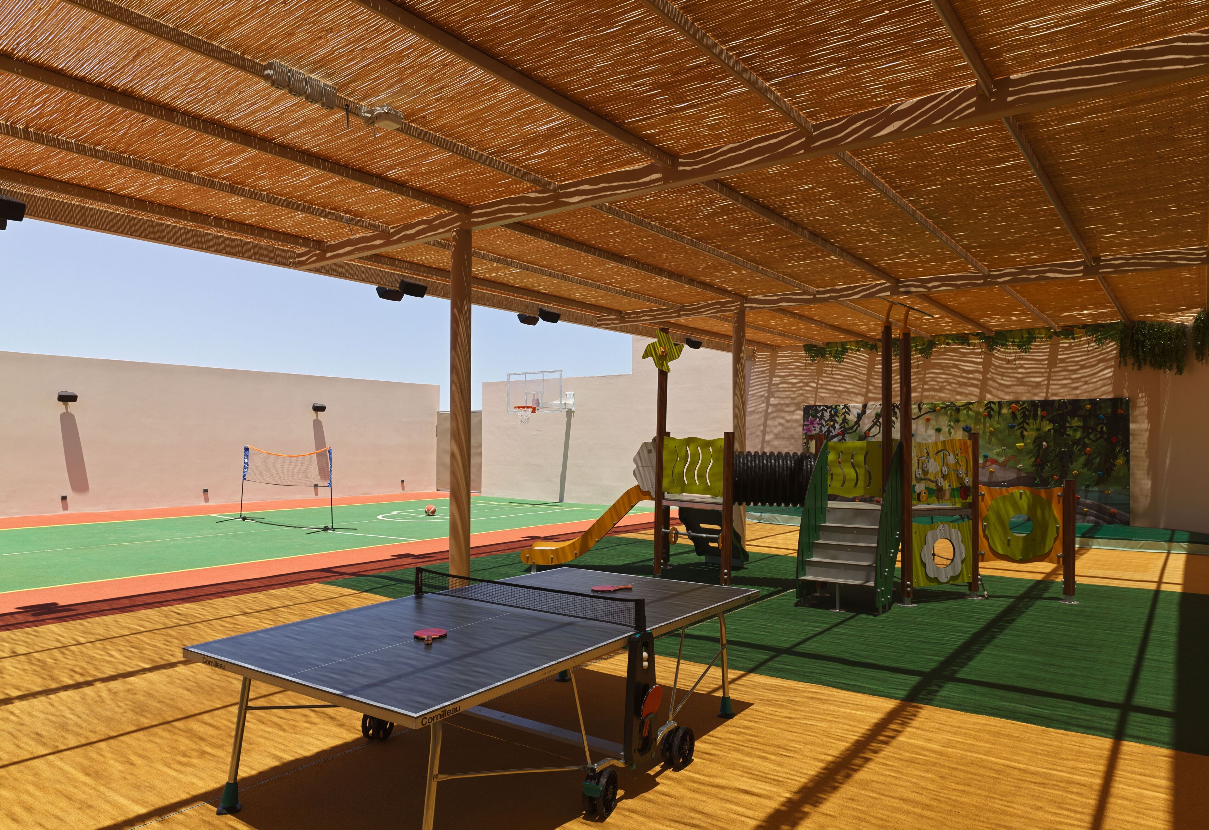 An indoor sports facility with a ping pong table, a basketball court, and a climbing wall.