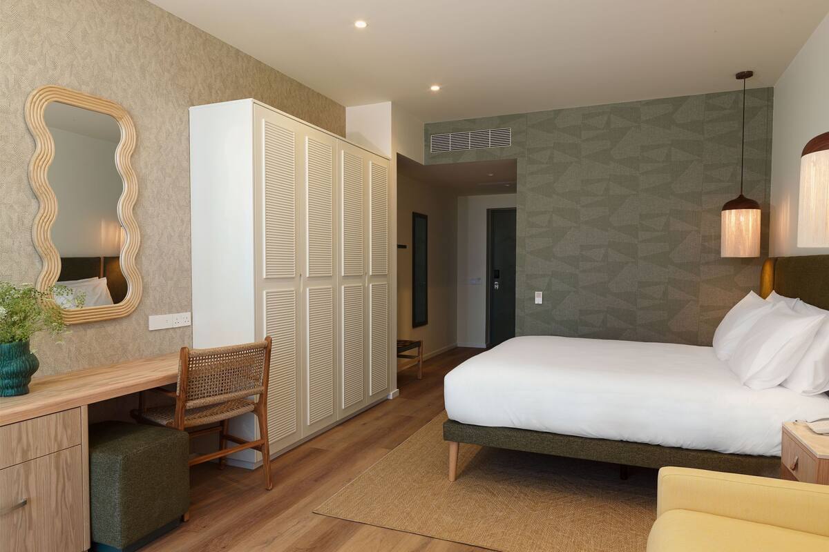 Una habitación de hotel con cama, escritorio, silla, armario y espejo.