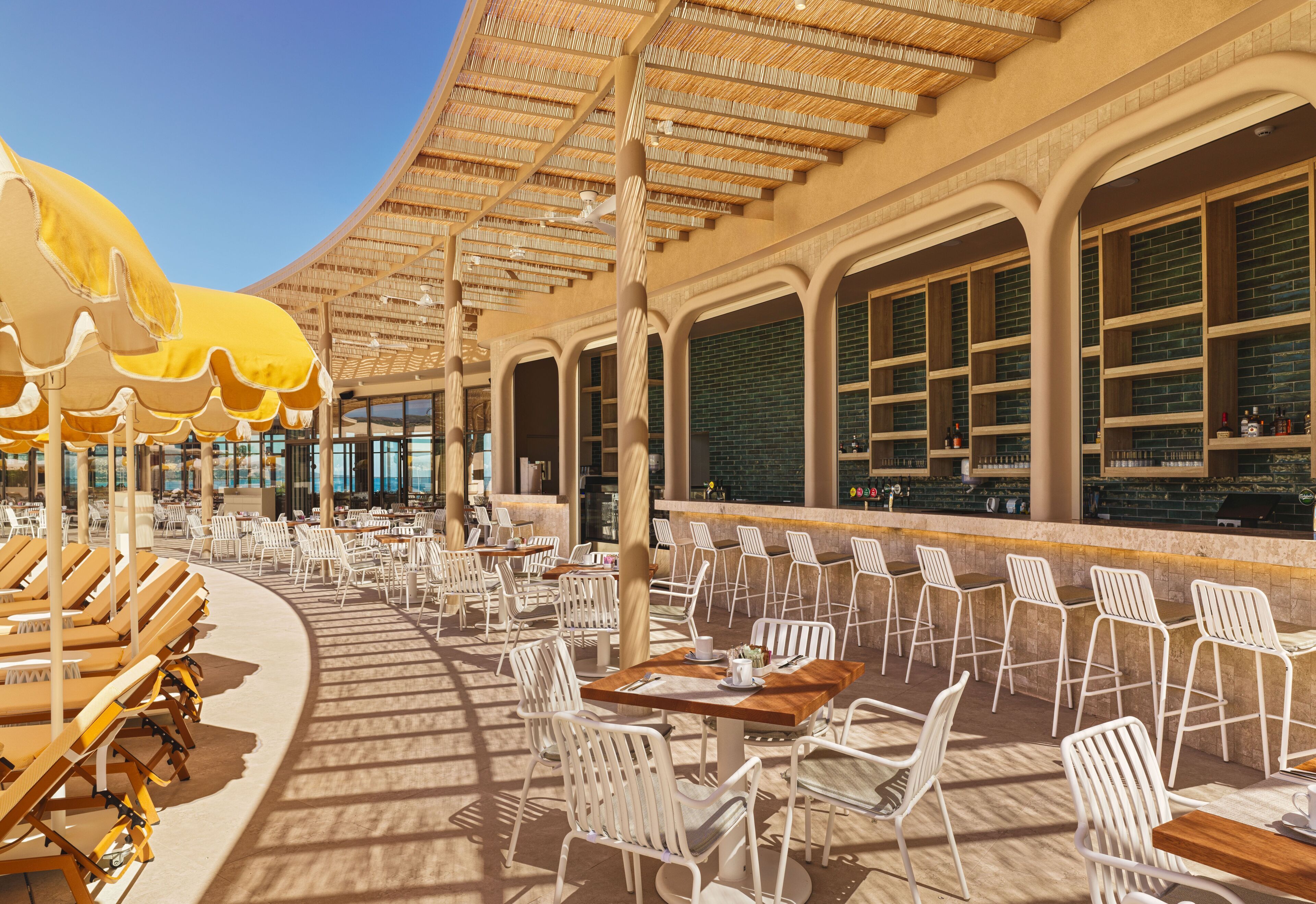 An outdoor seating area with tables and chairs, a bar area with shelves, and a covered section with umbrellas.
