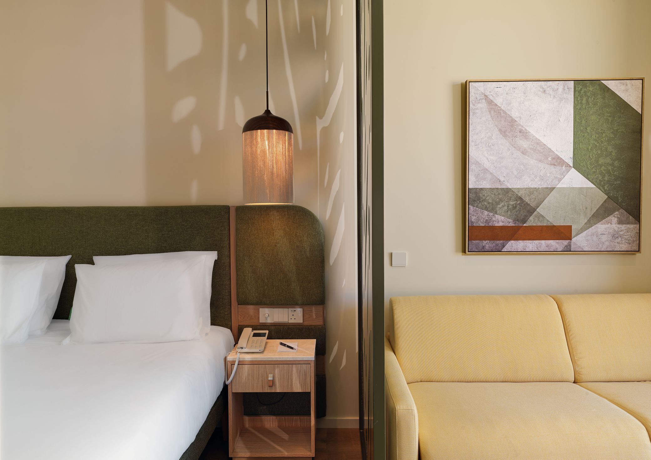 Camera d'albergo con un letto, un comodino con un telefono, una lampada, un divano e un'opera d'arte astratta appesa alla parete.
