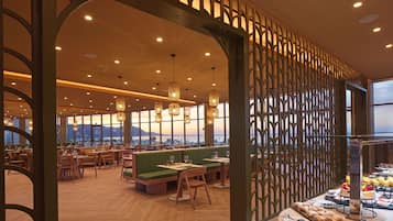 A restaurant interior with wooden flooring, green seating, and a view of the cityscape through large windows.