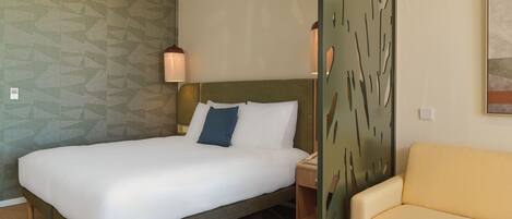 A hotel room with a bed, a bedside table, a lamp, a chair, and a decorative wall panel.