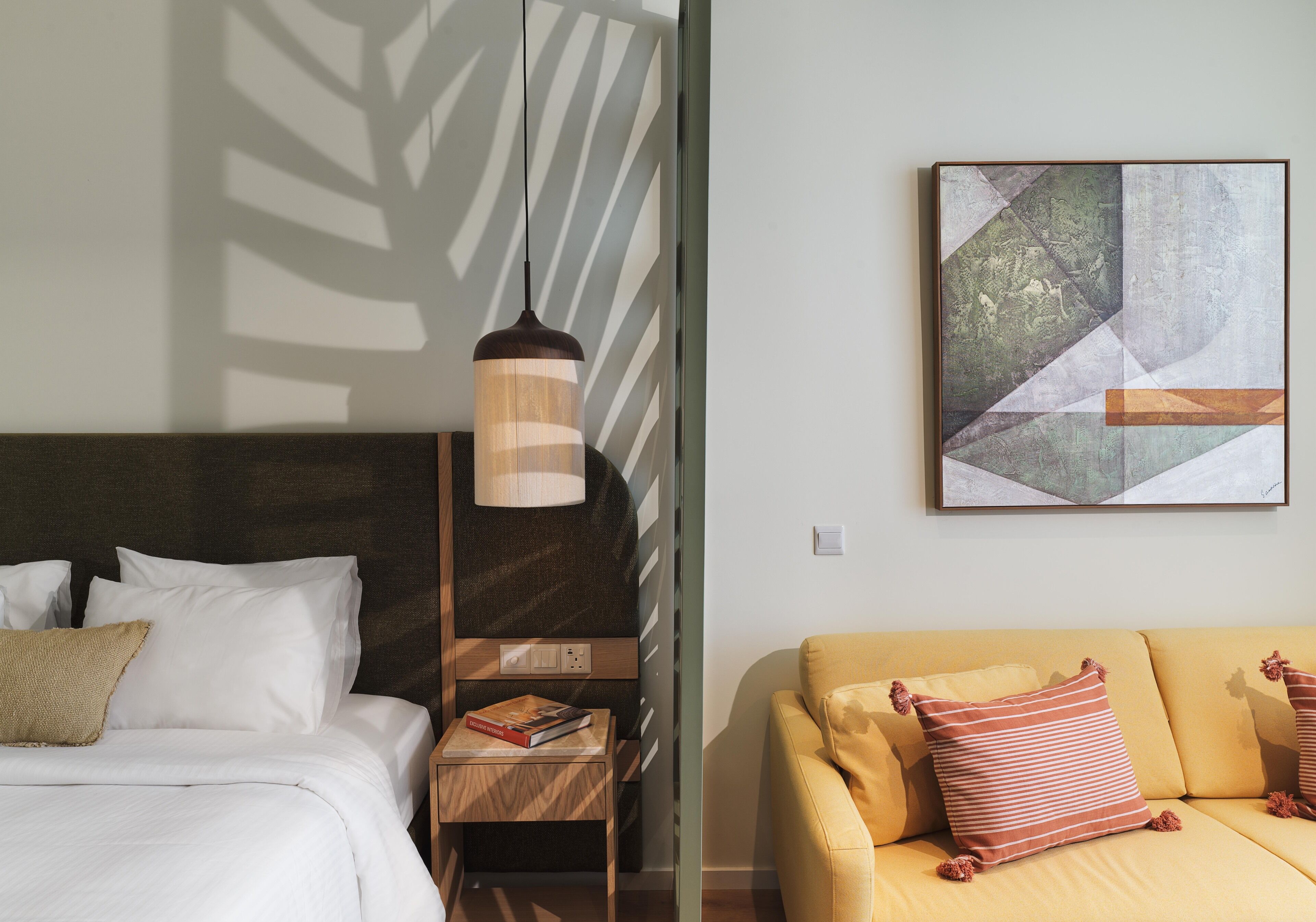 A hotel room with a bed, bedside table, lamp, and a sofa.