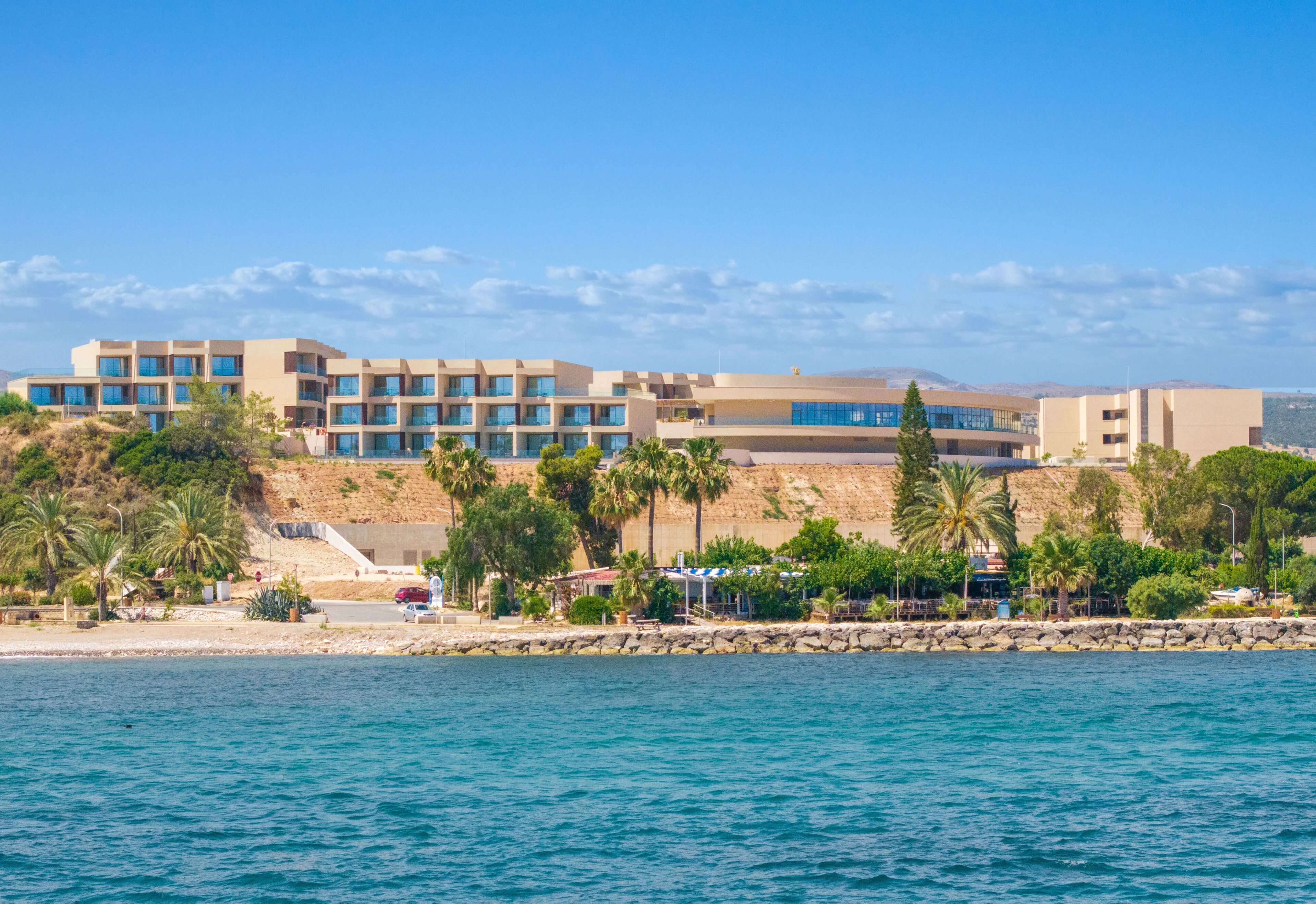 Un hotel frente al mar con varios pisos, costa rocosa y palmeras.