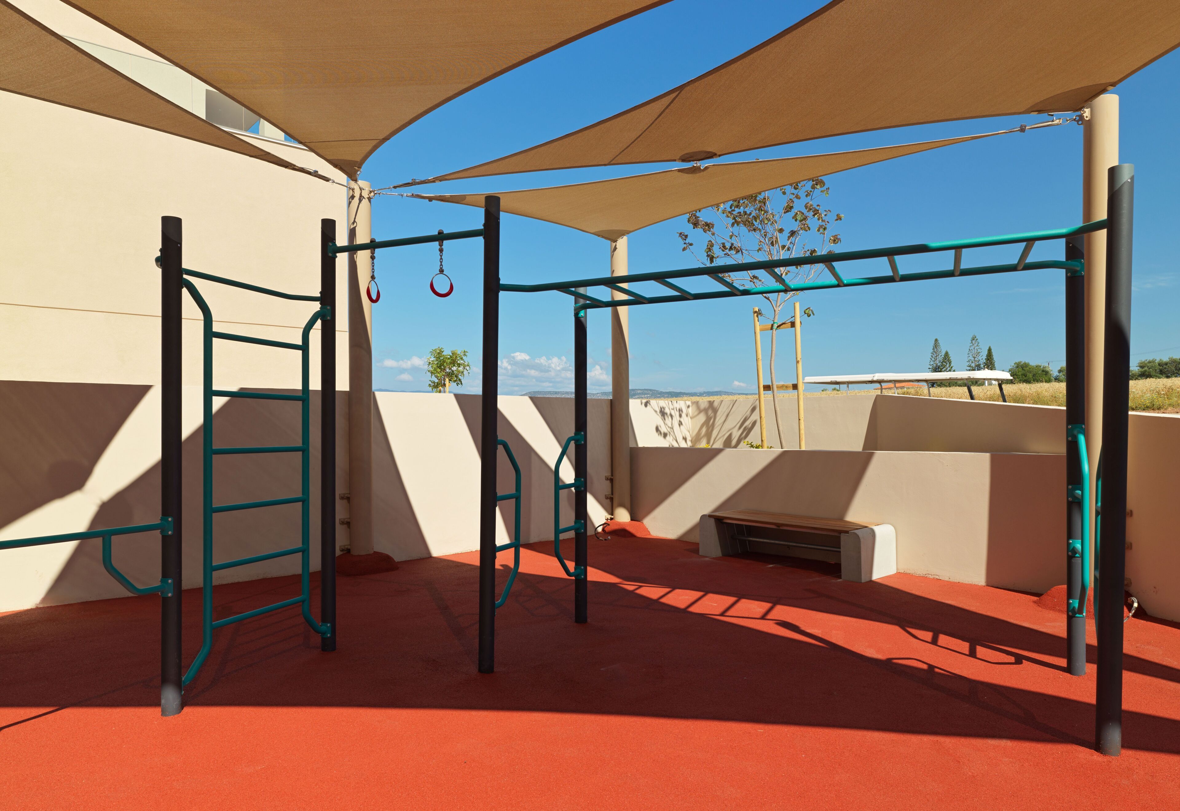 An outdoor play area with a climbing structure, a bench, and a shaded area.