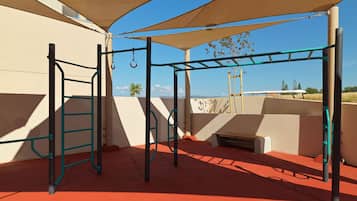 An outdoor play area with a climbing structure, a bench, and a shaded area.