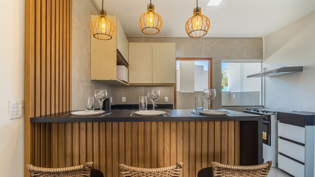 A modern kitchen with a central island, three hanging pendant lights, and three wicker chairs. - Apt in Condo w/ BBQ Area in Porto - BA MAA (Porto Seguro)