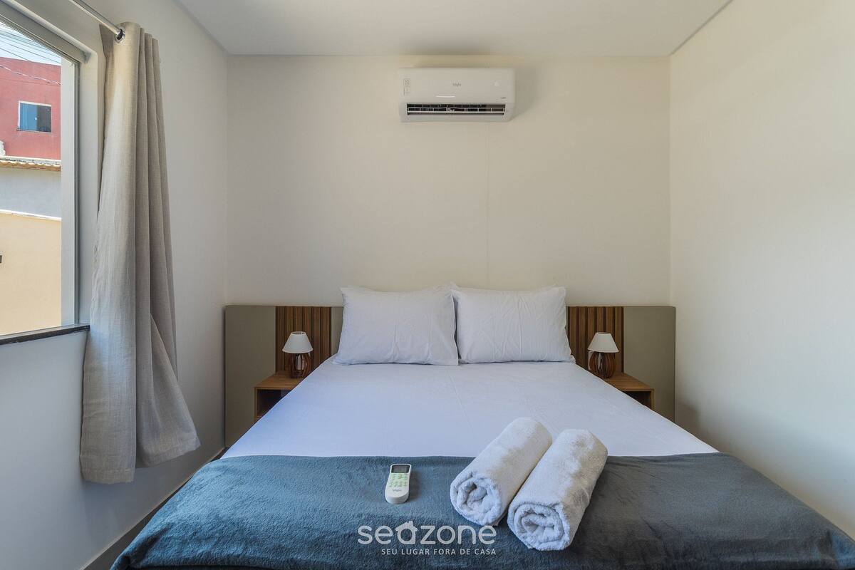 Une chambre d’hôtel avec un lit, deux lampes de chevet, une télécommande et une serviette enroulée.