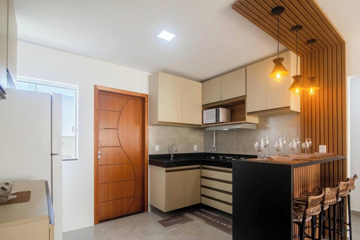 Une cuisine moderne avec une porte en bois, des placards intégrés, un plan de travail noir et un coin bar avec des tabourets.