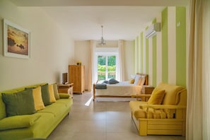 Ein Zimmer mit einem Bett, einem grünen Sofa, einem gelben Sessel, einem Holzschrank und einem Gemälde an der Wand.