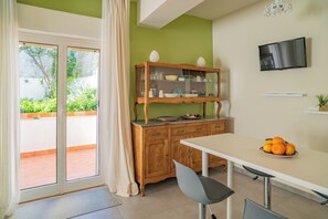Ein Essbereich mit Tisch, Stühlen, einer Holzschrank mit Glastüren, einem Fernseher und Blick ins Freie.