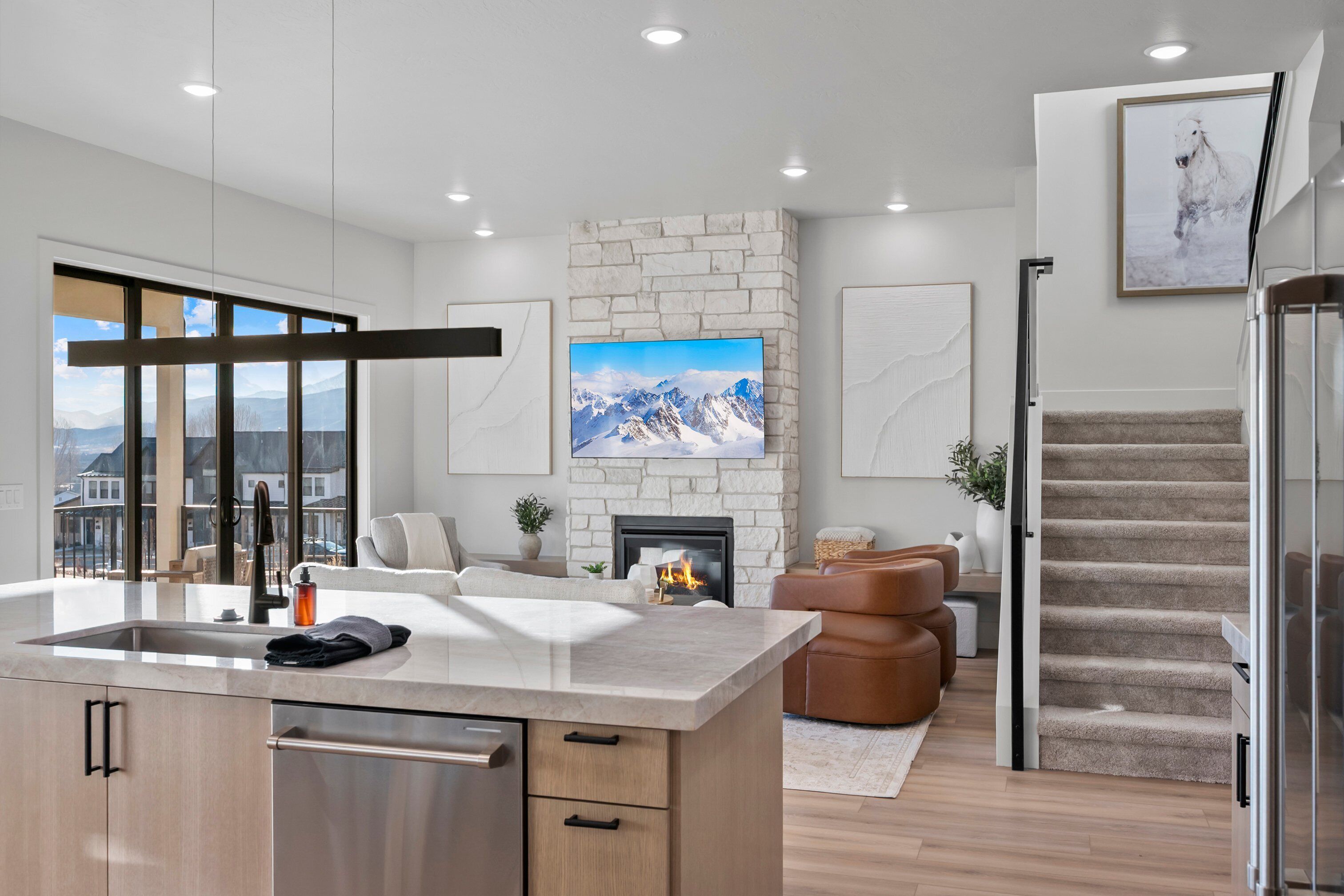 A modern kitchen with a large island, a fireplace, and a view of mountains through large windows.