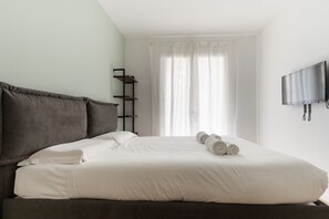 A neatly made bed with white linens, a dark headboard, and a TV mounted on the wall. - GuestHost - A comfortable and bright 55 square meters apartment, perfect for four people, located on the first floor of a building with an elevator (NOT accessible to disabled guests).The property is located in the Cascina Merlata neighborhood, a growing (Milan)