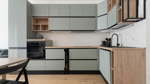 Eine kompakte Küche mit integrierten Geräten, einem Holztisch und einem schwarzen Stuhl.
