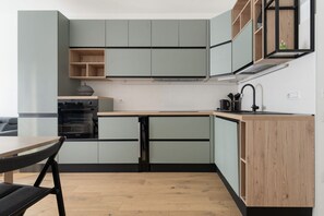 A compact kitchen with built-in appliances, a wooden dining table, and a black chair. - GuestHost - A comfortable and bright 55 square meters apartment, perfect for four people, located on the first floor of a building with an elevator (NOT accessible to disabled guests).The property is located in the Cascina Merlata neighborhood, a growing (Milan)