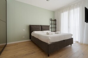 Une chambre à coucher comprenant un lit, une table de chevet, un téléviseur fixé au mur et une fenêtre avec des rideaux.