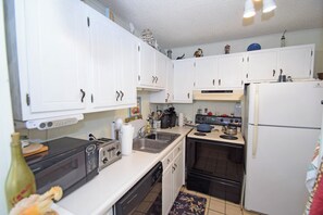 A compact kitchen with white cabinets, a microwave, a toaster, a sink, and a stove. - Bridgepoint II 201A - Ocean City, MD (Ocean City)
