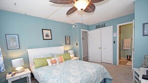 Ein Schlafzimmer mit Bett, Nachttischen, einem Deckenventilator und einer Tür mit der Aufschrift 'RELAX'.