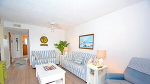 Ein Wohnzimmer mit einem weißen Couchtisch, gestreiften Sofas, einem blauen Sofa, einem Deckenventilator, einem gerahmten Bild und einer Topfpflanze.
