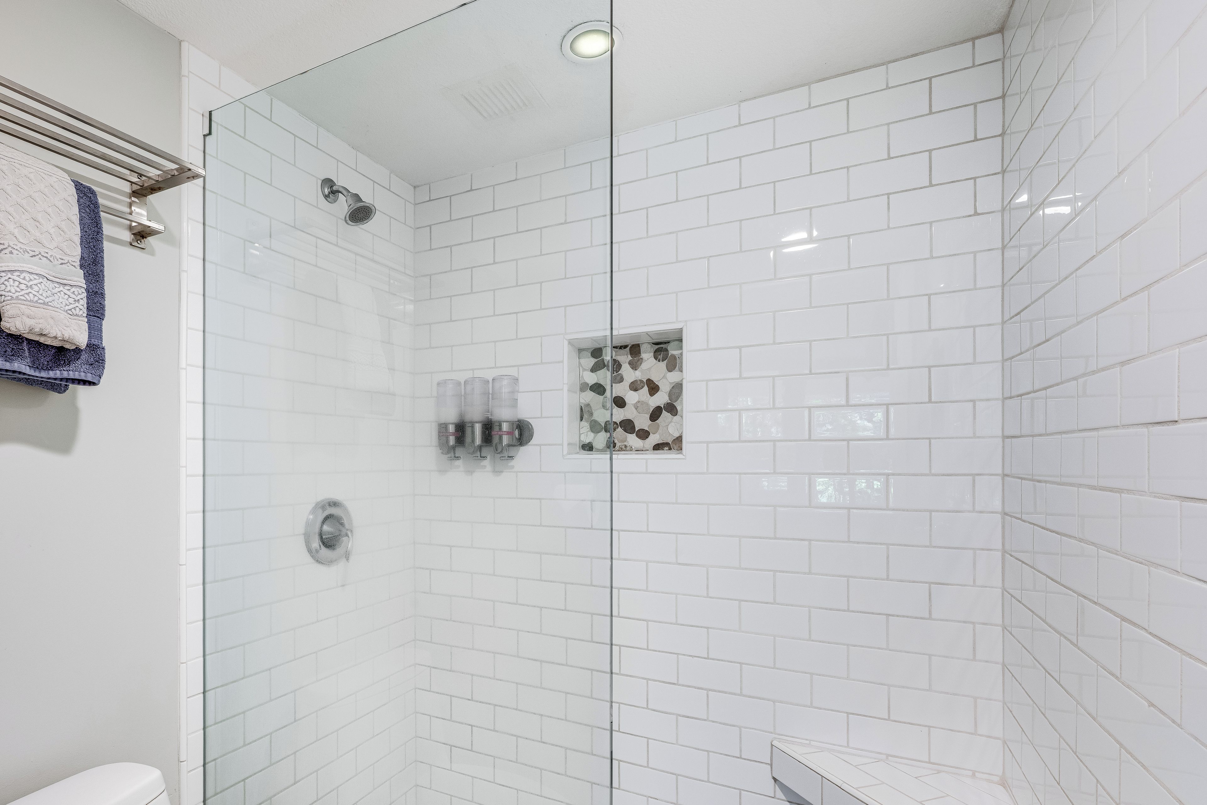 Ein modernes Badezimmer mit weißen, rechteckigen Fliesen, einer Glastrennwand-Dusche und einer kleinen, dekorativen Fliesenfassade an der Wand.