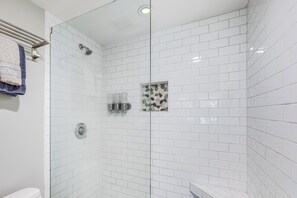 Ein modernes Badezimmer mit weißen, rechteckigen Fliesen, einer Glastrennwand-Dusche und einer kleinen, dekorativen Fliesenfassade an der Wand.