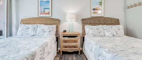 Una habitación con dos camas, una mesita de noche con lámpara y decoración en la pared que representa escenas de playa.