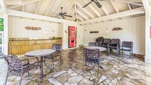 Uma área externa coberta com piso de pedra, uma cozinha com armários de madeira e uma geladeira Coca-Cola.