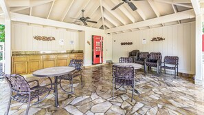 Un espacio exterior techado con suelo de piedra, una cocina con armarios de madera y un refrigerador Coca-Cola.