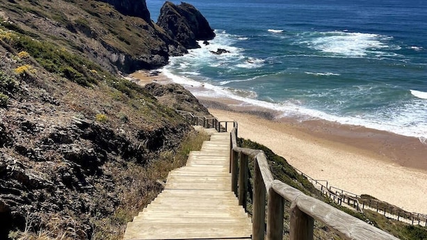 Eine Holztreppe führt zu einem Strand mit felsigen Klippen hinab.