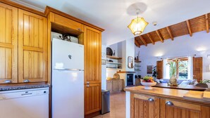 Une cuisine avec des meubles de rangement en bois, un réfrigérateur blanc et un îlot central en bois sur lequel se trouve un saladier rempli de fruits.