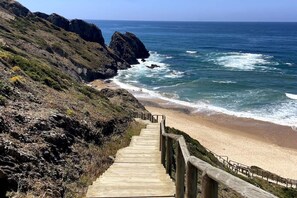Un escalier en bois descend vers une plage bordée de falaises rocheuses.