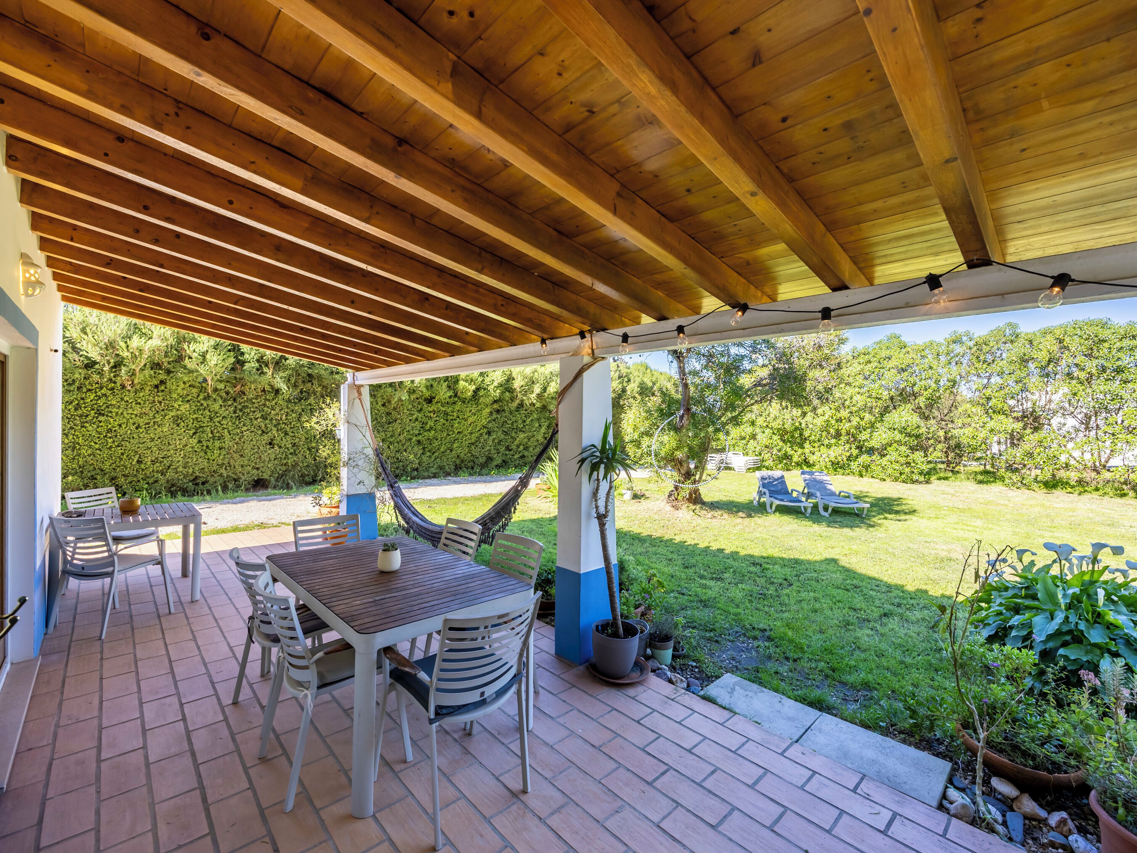 Een overdekt terras met een houten plafond, een tafel met stoelen en een hangmat.