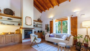 A cozy living room with a fireplace, wooden beams, a sofa, and a view of greenery through a window. - Quintinha Mojud - Lavanda Room (Rogil)