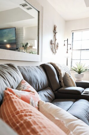 Ein modernes Wohnzimmer mit einem Ecksofa, einem großen Spiegel und einer Topfpflanze.
