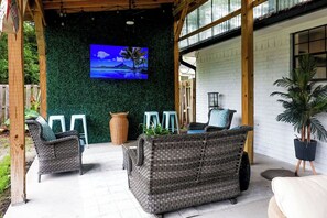 Ett takförsett utomhusområde med sittplatser, möbler av rotting, en tv-skärm och en vit tegelvägg.
