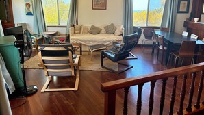 A spacious living room with a sofa, a dining table, and a large window with curtains.