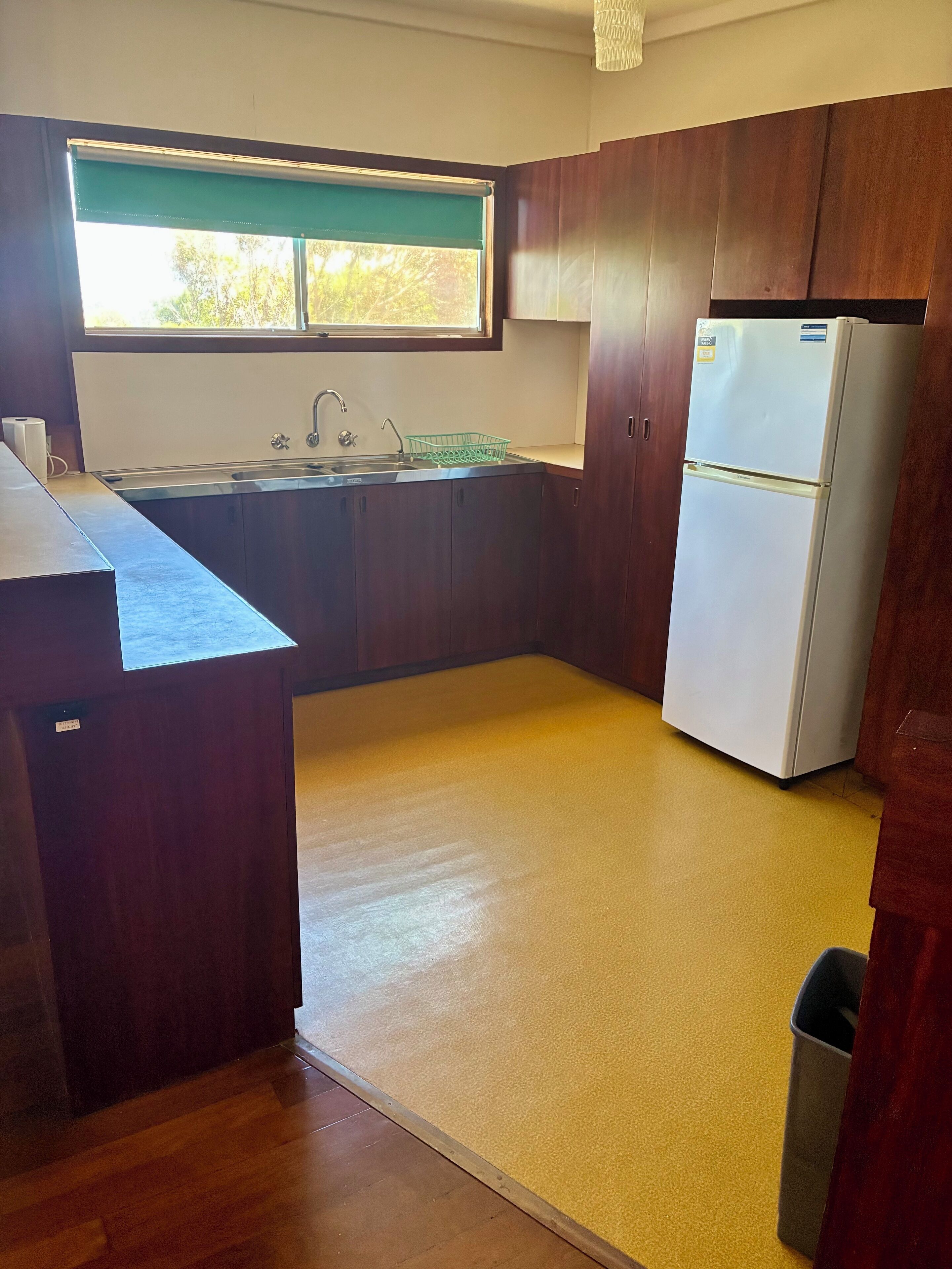 A kitchen with wooden cabinets, a sink, a refrigerator, and a window with a view of trees.