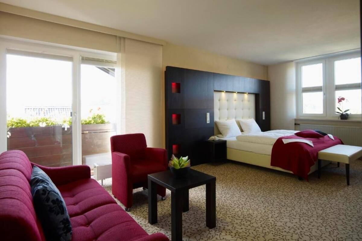 Ein Hotelzimmer mit einem Bett, einem roten Sofa, einem kleinen Tisch und einem Fenster mit Blick ins Freie.