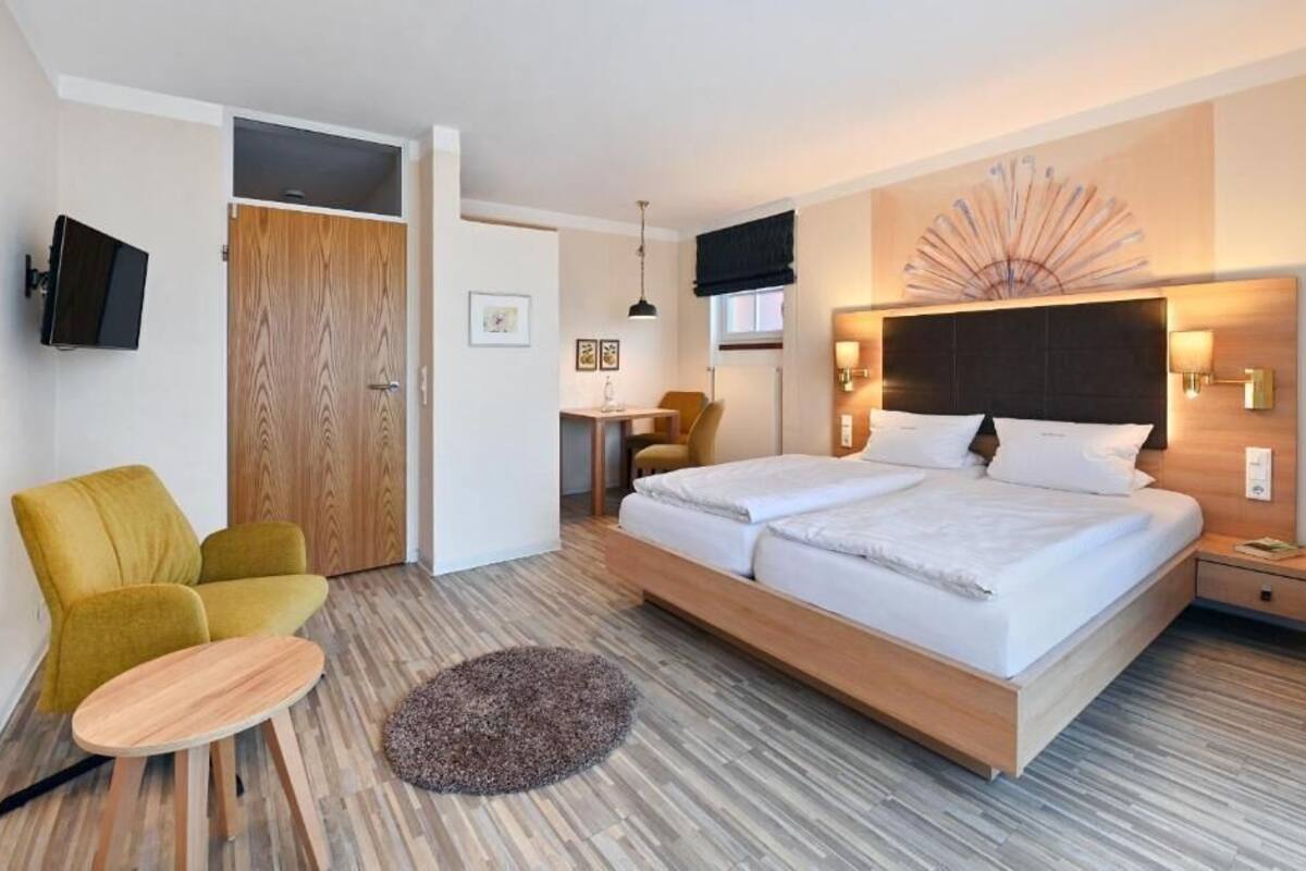 Ein modernes Hotelzimmer mit einem großen Bett, einem Schreibtisch, einem Sessel und einem Fernseher.