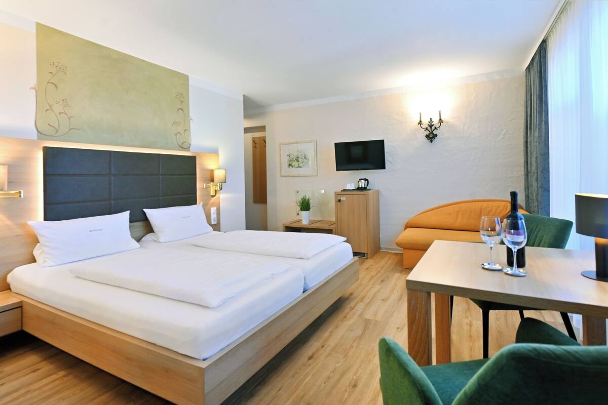 Ein Hotelzimmer mit einem großen Bett, einem Schreibtisch mit Stuhl, einem Fernseher und einem kleinen Schrank.