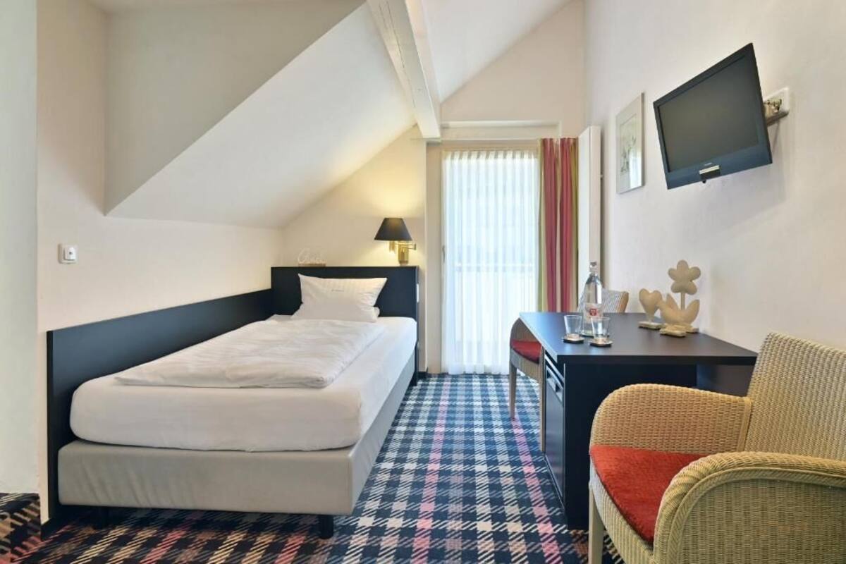 Ein Hotelzimmer mit Bett, Schreibtisch, Stuhl, Fernseher und einem Fenster mit Vorhängen.