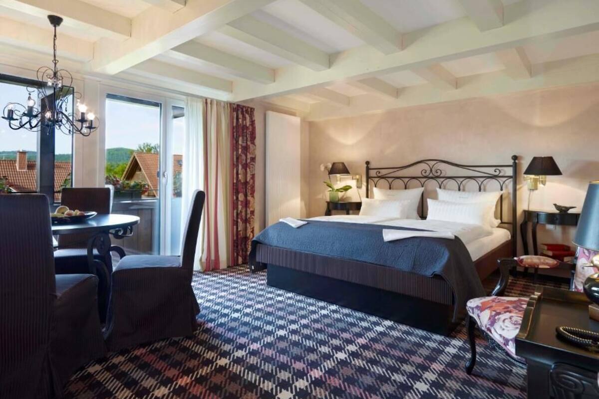Ein Hotelzimmer mit Bett, Schreibtisch, Stuhl, einer Kronleuchter und Blick nach draußen.