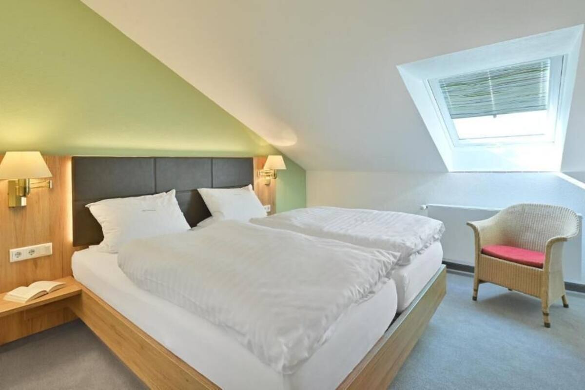 Ein modernes Hotelzimmer mit einem großen Bett, einem kleinen Sessel und einem Oberlicht.