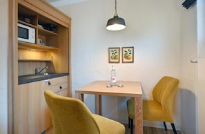 Cocina compacta con microondas, estanterías y una mesa con sillas. Hay dos cuadros en la pared.