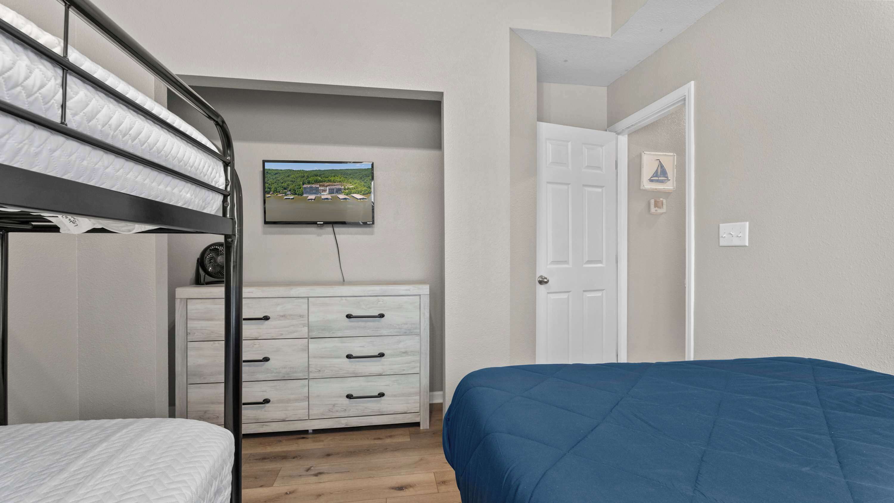 A bedroom with bunk beds, a dresser, a television, and a door.