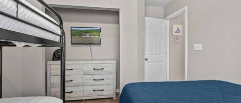 A bedroom with bunk beds, a dresser, a television, and a door.