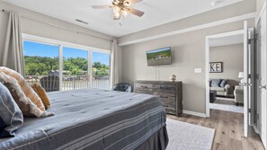 A bedroom with a large bed, a dresser, a television, and a view of a lake through the window.
