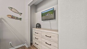 Habitació amb televisió penjada a la paret, un taulell de fusta amb calaixos i dos peixos decoratius a la paret.