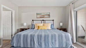 A bedroom with a bed, two nightstands, a wall-mounted lamp, a window with curtains, and a poster on the wall.