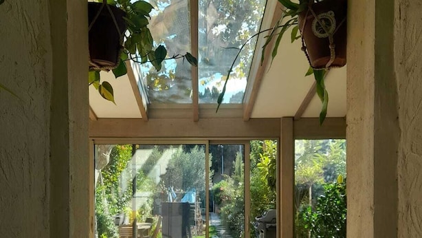 Una habitación soleada con un sofá amarillo, una mesa de centro blanca y vistas a un jardín a través de puertas de cristal amplias.